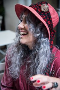 Grey hair model Valeria Sechi laughing and wearing pink hat and dress