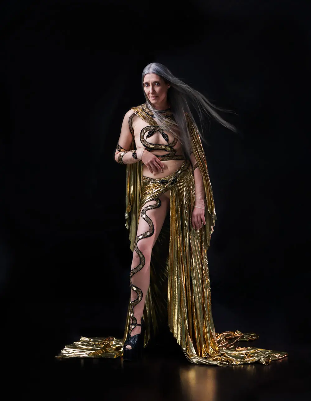 Valeria Sechi in abito da sera Gucci per un editoriale fashion — modella over 50 dai capelli grigi naturali in couture oro con motivo Medusa
