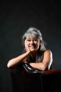 A portrait of grey hair model Valeria Sechi sitting on a leather armchair