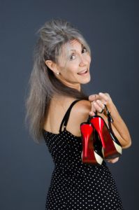 A portrait of grey hair model Valeria Sechi with a pois dress and red shoes in hand