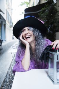 Grey hair model Valeria Sechi laughing and wearing gloves and a hat with feathers