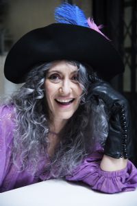 Grey hair model Valeria Sechi smiling and wearing gloves and a hat with feathers