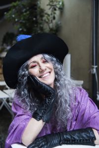 Grey hair model Valeria Sechi smiling and wearing gloves and a hat with feathers