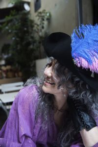 Grey hair model Valeria Sechi smiling and wearing gloves and a hat with feathers