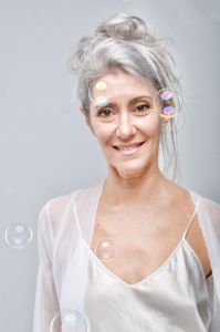 Italian grey hair model Valeria Sechi in white dress behind soap bubbles