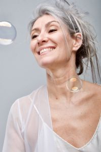Italian grey hair model Valeria Sechi in white dress behind soap bubbles