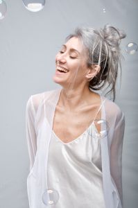 Italian grey hair model Valeria Sechi in white dress behind soap bubbles