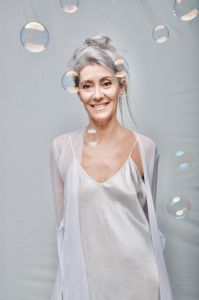 Italian grey hair model Valeria Sechi in white dress behind soap bubbles