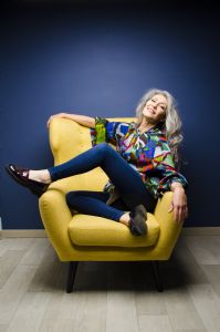 Italian grey hair model Valeria Sechi with a colorful shirt on a yellow sofa.